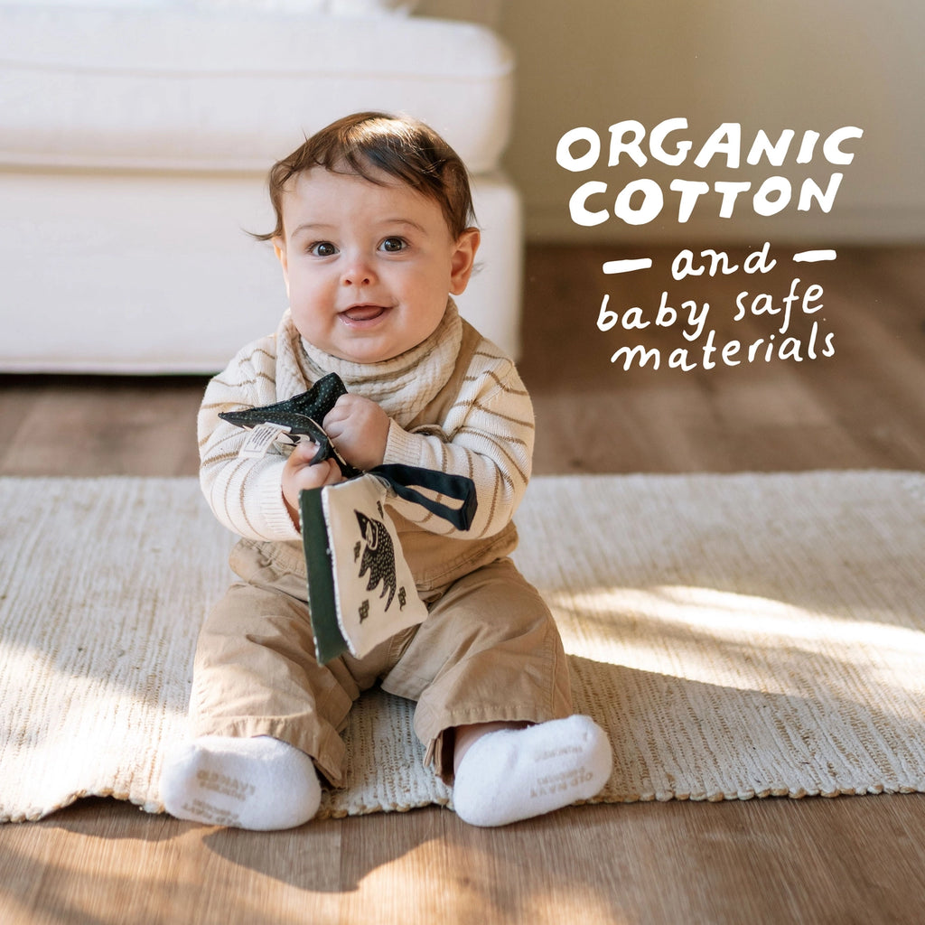 Baby sitting on a wooden floor holding a book, with text about organic cotton and baby safe materials.